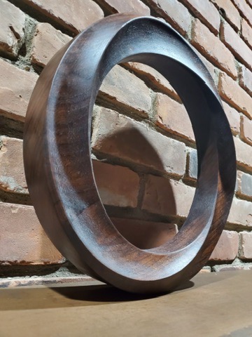 Circular ring sculpture in carved wood with concentric relief detail, standing on base