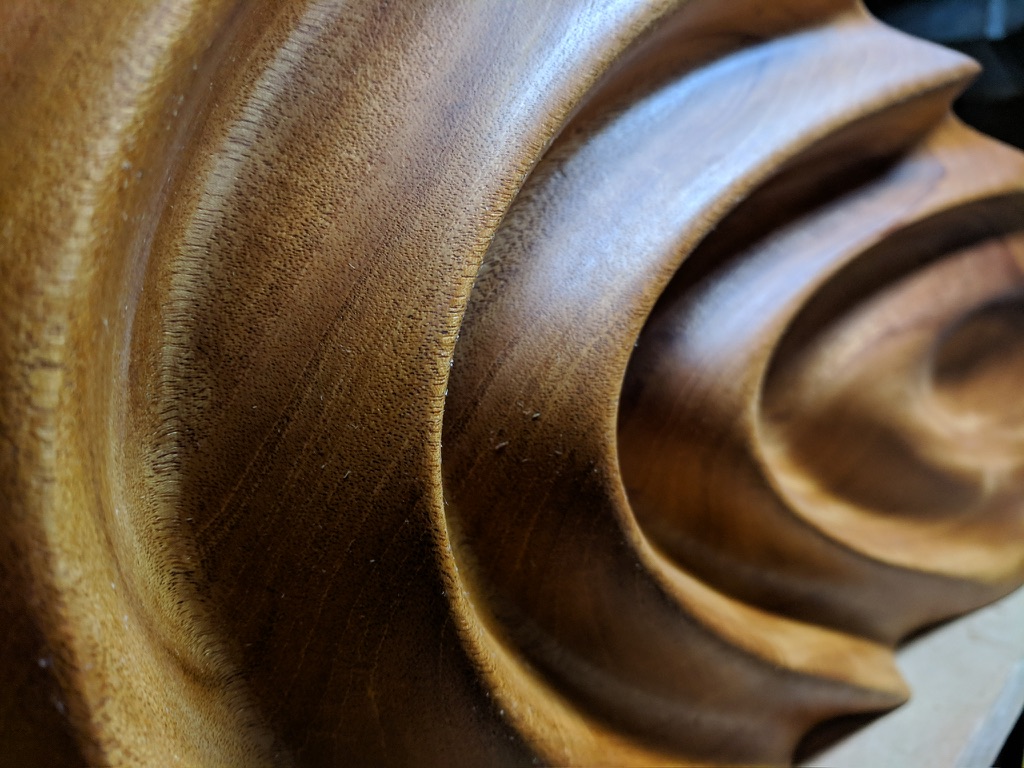 Macro detail of CNC-carved spiral relief in wood, showing precise tool depth and grain texture