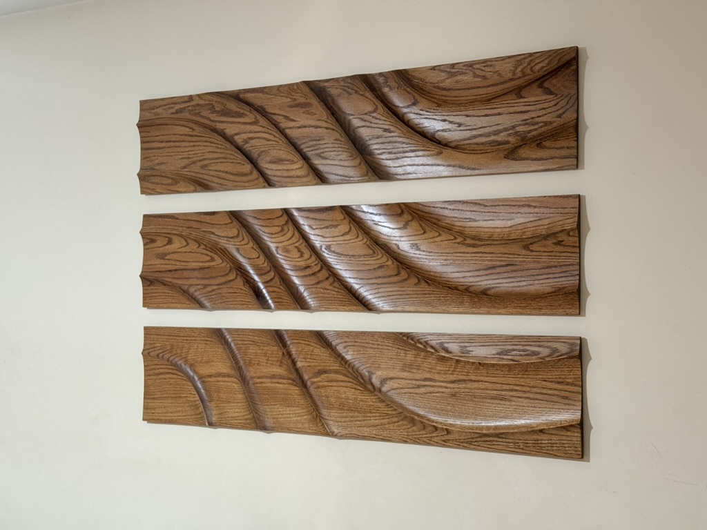 Three large CNC-carved wood panels installed on wall, layered geometric relief pattern in natural finish